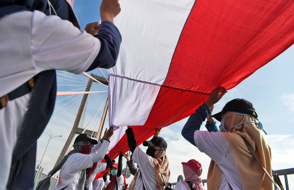Warga berusaha membentangkan bendera merah putih sepanjang Jembatan Suramadu saat puncak 'Millenial Road Safety Festival' di Jembatan Suramadu, Surabaya, Jawa Timur, Minggu (17/3/2019).