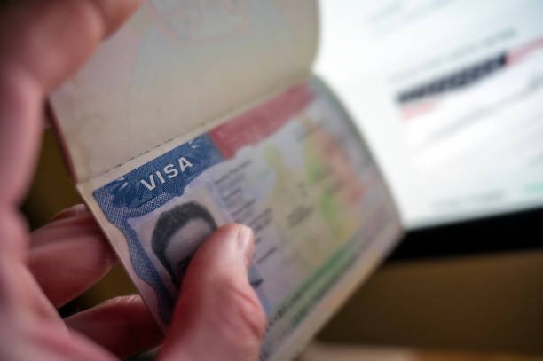 Visa H-1B dalam paspor yang sedang dibuka di depan komputer, simbol kebijakan imigrasi Amerika Serikat.